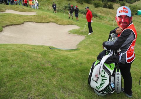 Game face: Thomas Bjorn's caddie got into the spirit of the day by donning a mask while his employer tried to get out of bunker at the par-3 16th